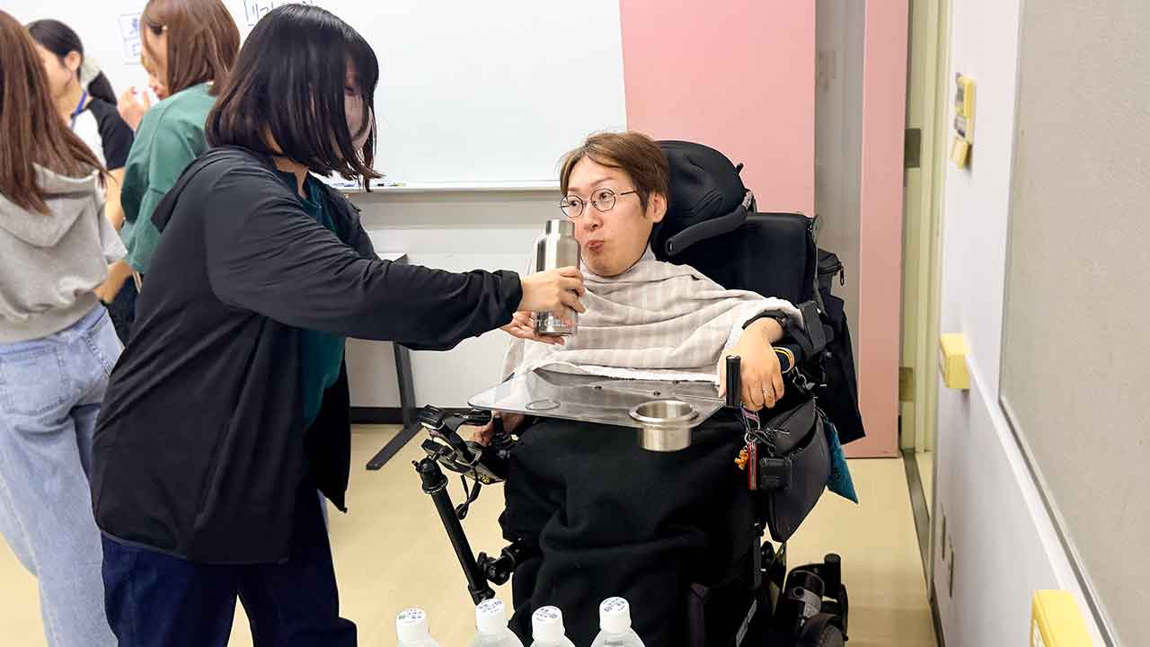 飲み物を口元へ運ぶ飲料介助を学生が体験している様子