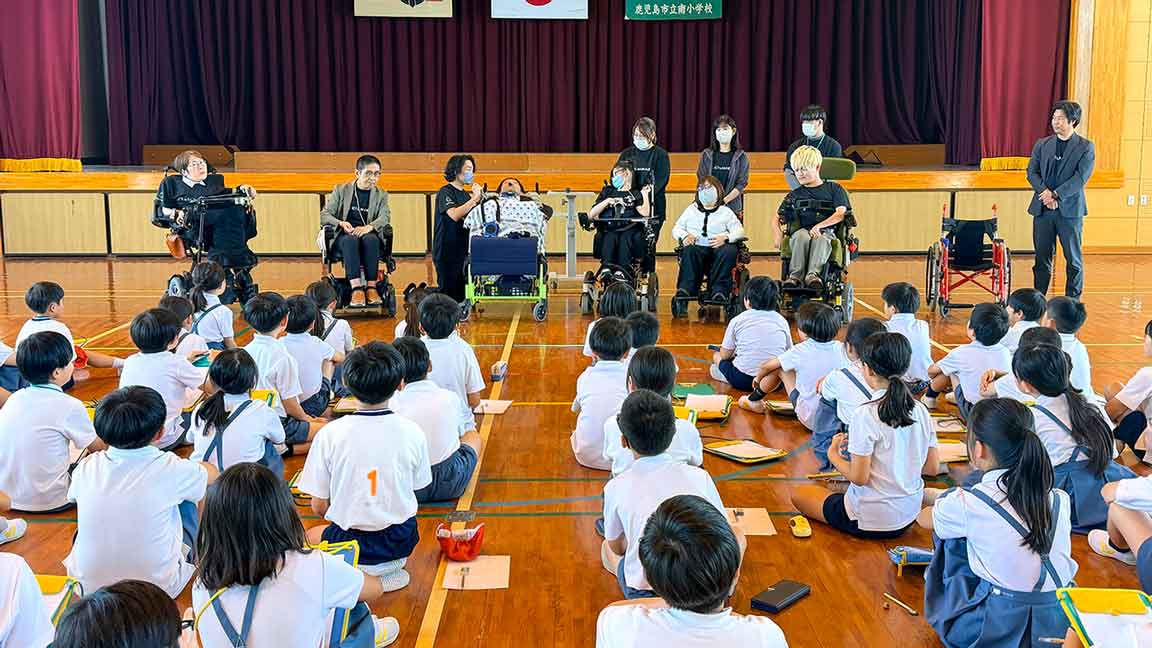 鹿児島市立南小学校の体育館で、CILひかりの当事者スタッフが車いすでの暮らしについて話し、児童が聞き入る様子